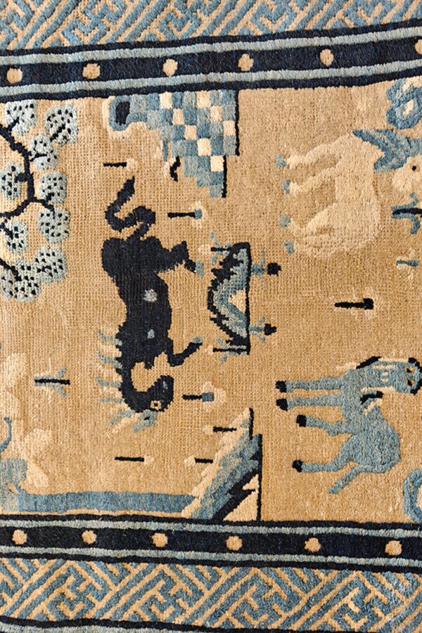 Detail of a low-pile tan rug with blue stylized horses, trees, and dark blue patterned geometric borders.