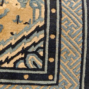 Close-up of a tan, slate blue, and dark blue rug showing geometric and floral border patterns with a medium pile.