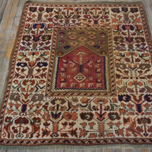 Low-pile rug with complex floral and geometric patterns in red, ivory, and olive green on distressed wood.