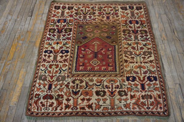 Low-pile rug with complex floral and geometric patterns in red, ivory, and olive green on distressed wood.