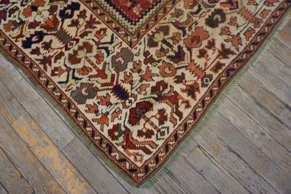 Intricate traditional rug corner in cream, rust, and blue resting on distressed gray plank flooring.