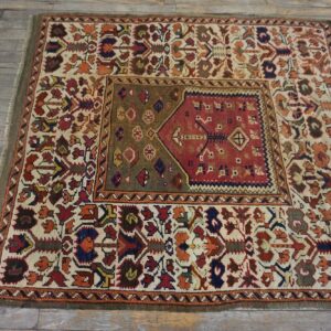 Low pile rug featuring complex red, ivory, and olive geometric designs resting on distressed gray wood flooring.