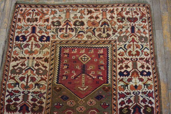 Geometric pattern rug in cream, red, orange, and navy colors displayed on rustic wooden flooring.