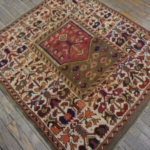 A small, low-pile rug with a red and olive geometric medallion rests on weathered gray wooden floors.