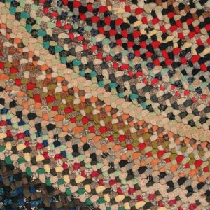 Multicolored braided rug texture showing diagonal stripes of red, tan, black, green, and blue patches.