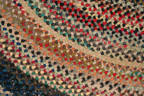 Multicolored braided rug texture showing diagonal stripes of red, tan, black, green, and blue patches.