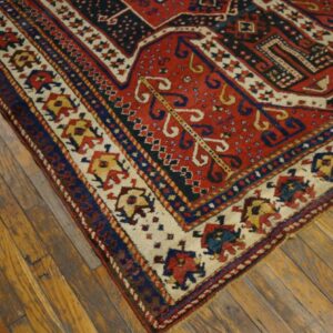 Corner of a red, blue, and cream geometric rug with low pile on distressed wood planks.