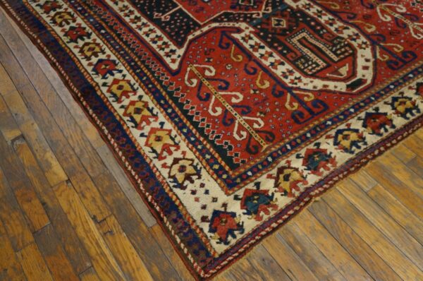 Corner of a red, blue, and cream geometric rug with low pile on distressed wood planks.