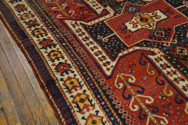 Geometric red and dark blue rug showing borders with stylized figures rests on aged wood plank flooring.