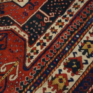 Red, navy, and cream high-pile rug with complex geometric patterns lying on hardwood flooring.