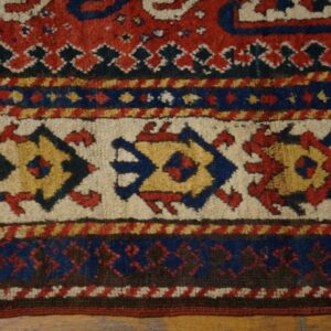 Red, blue, cream, and yellow tribal rug border with geometric medallions on wood floor.