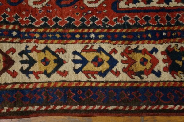 Red, blue, cream, and yellow tribal rug border with geometric medallions on wood floor.