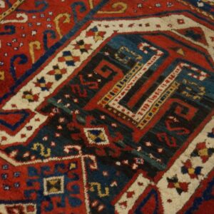 Close-up of a high-pile geometric rug in red, dark blue, ivory, and black, featuring complex tribal motifs.