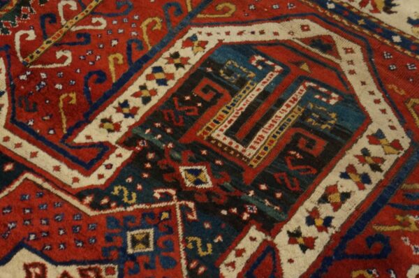 Close-up of a high-pile geometric rug in red, dark blue, ivory, and black, featuring complex tribal motifs.