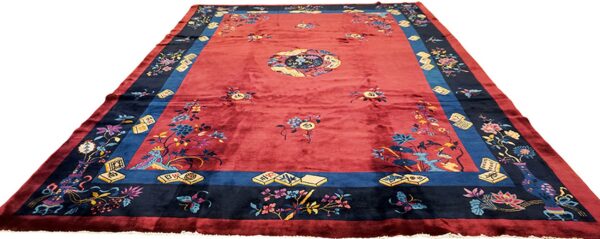Traditional style red rug featuring a contrasting navy border filled with intricate floral and symbolic patterns.