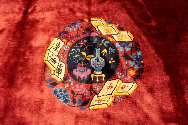Plush red rug featuring a circular motif of a vase, flowers, and yellow mahjong tiles.