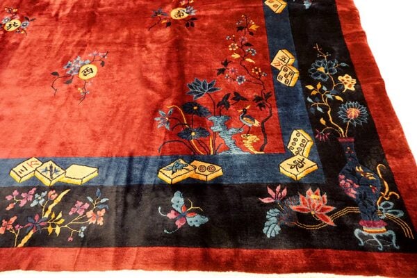 Rust-red rug with ornate navy and black borders decorated with flowers, birds, and game tiles.