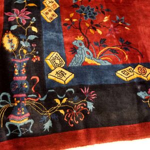 Ornate red rug corner detailed with black, blue, and yellow floral motifs, vases, and mahjong tiles.