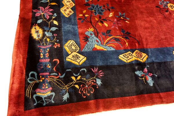 Ornate red rug corner detailed with black, blue, and yellow floral motifs, vases, and mahjong tiles.