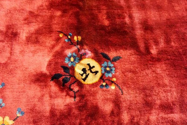 The plush red pile rug shows a detailed design of blue flowers and a yellow circular symbol.