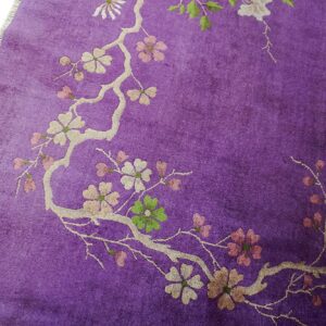A close-up of a vibrant purple rug featuring a blossoming branch pattern in cream, pink, and green.