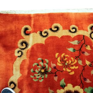 Orange rug detail with bright floral patterns and a gold scrolled border; white fringe is visible.