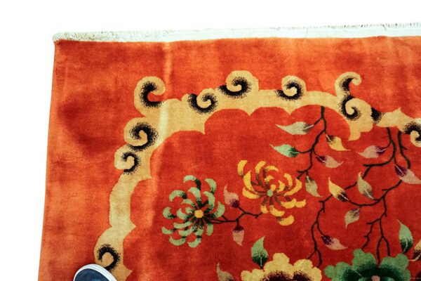 Orange rug detail with bright floral patterns and a gold scrolled border; white fringe is visible.