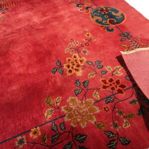 Deep rose pink rug with floral and medallion motifs in teal and gold, folded to show the backing.