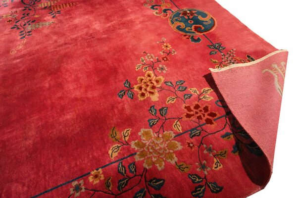 Deep rose pink rug with floral and medallion motifs in teal and gold, folded to show the backing.