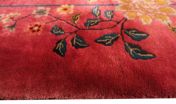 Close-up of a deep red plush rug featuring a floral pattern with gold, cream, and teal leaves.