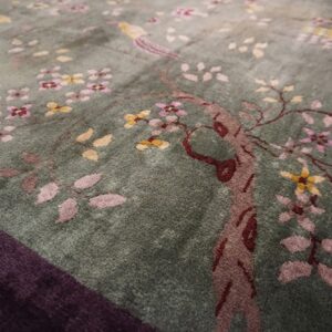 Sage green rug with a pink and yellow floral motif, featuring a bird and a dark purple border.