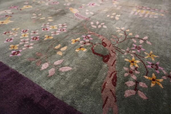 Sage green rug with a pink and yellow floral motif, featuring a bird and a dark purple border.