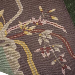 A tightly woven brown rug with stylized botanical patterns in yellow and pink overlays a deep green rug.