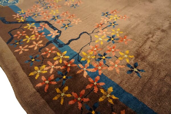 Brown rug with a stylized tree branch, blue stream, and colorful scattered yellow, coral, and blue blossoms.