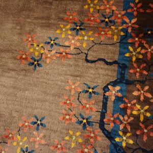 Plush brown rug featuring a stylized design of orange, yellow, and blue flowers on dark branches.