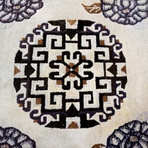 Detail of a cream medium-pile rug featuring a geometric black and brown interlocking medallion pattern.