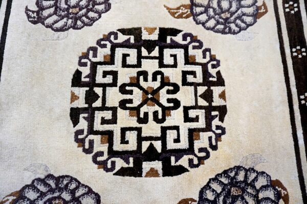 Detail of a cream medium-pile rug featuring a geometric black and brown interlocking medallion pattern.