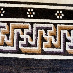 Close-up of a rug border showing interlocking geometric designs and small flowers in cream, tan, and dark colors.
