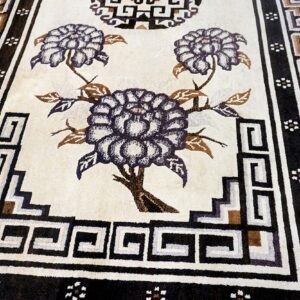 Textured cream rug with dark purple floral patterns and complex geometric borders in black and brown.