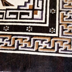 Plush black rug border framed by cream, tan, and purple interlocking geometric designs.