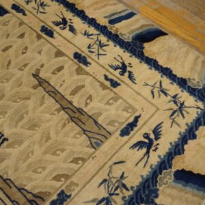 Tan rug with textured pile features dark blue dragons, birds, and border details, resting on wooden planks.