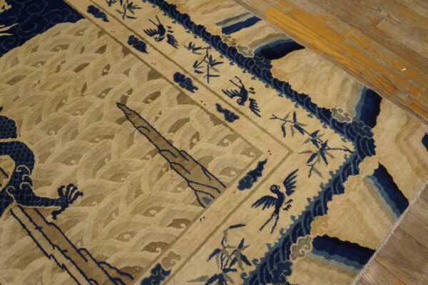 Tan rug with textured pile features dark blue dragons, birds, and border details, resting on wooden planks.