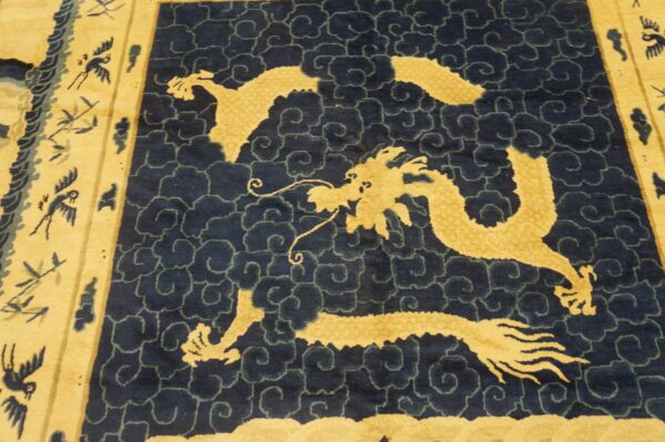 Blue rug with a golden dragon and cloud pattern bordered by stylized birds and light yellow field.