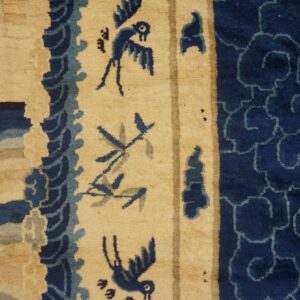 A close-up of a blue and beige rug showing stylized birds, undulating waves, and repeating cloud patterns.