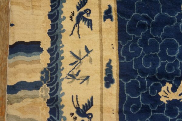 A close-up of a blue and beige rug showing stylized birds, undulating waves, and repeating cloud patterns.