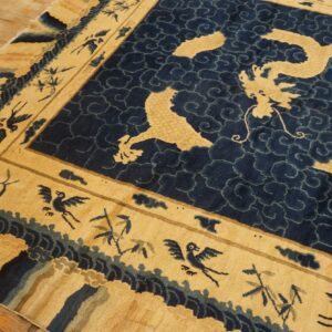 Plush tan and indigo rug featuring a dragon medallion and bird-filled wide border on wood floors.