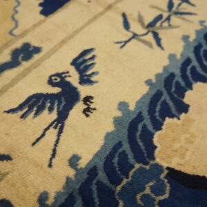 Detail view of a rug showing blue bird, wave, and bamboo patterns on a cream and tan field.