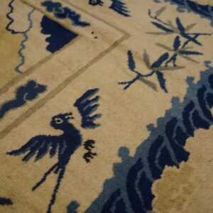 Traditional tan rug with visible pile texture and deep blue stylized bird and vine motifs.