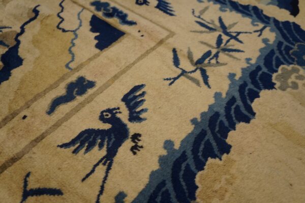 Traditional tan rug with visible pile texture and deep blue stylized bird and vine motifs.