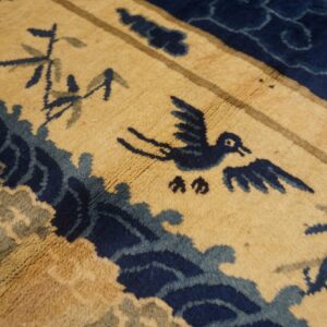Close-up of a gold rug featuring a navy blue bird and stylized waves in medium pile.